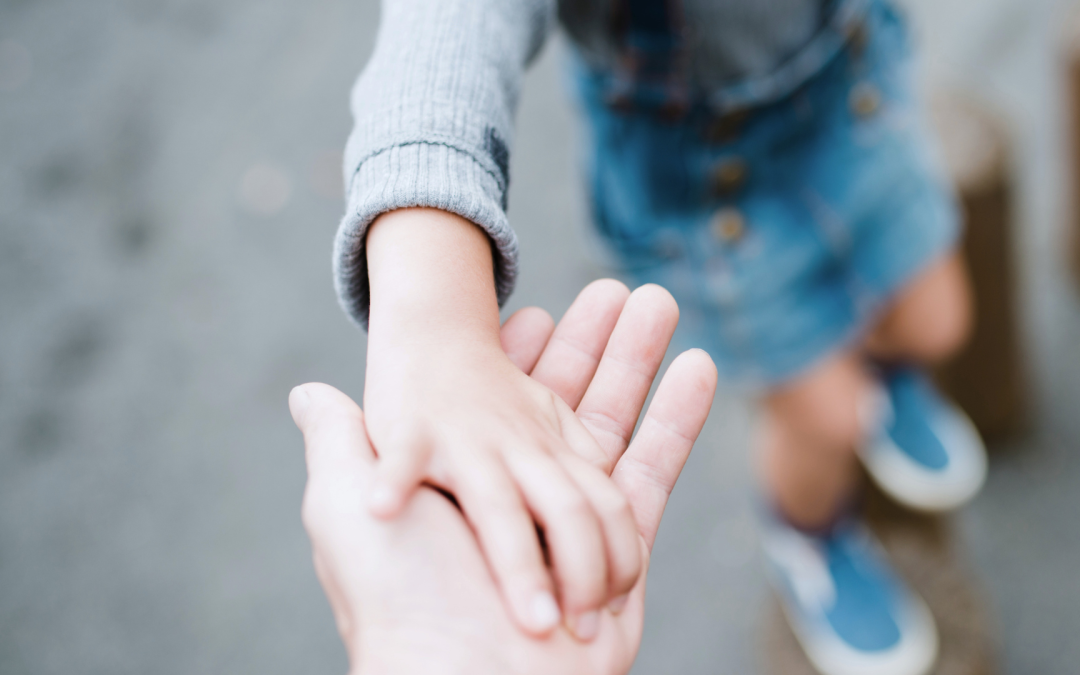 An adult hand holding a young child by the hand